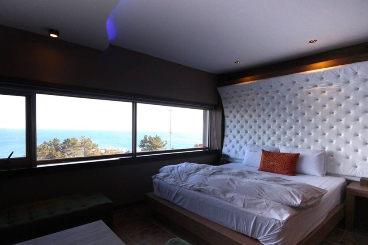 A bedroom with a large window, a tufted headboard, and a bed with white bedding.
