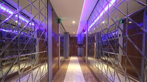 Un passadís amb parets de mirall i il·luminació morada que condueix a una porta amb un senyal de sortida verd.