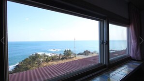 Habitació amb una finestra gran que ofereix vista al mar i a una costa rocosa.