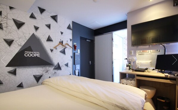 A hotel room with a bed, a desk with a computer, a TV, and a wall with geometric patterns.