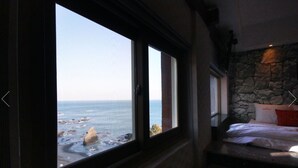 Habitació amb una finestra gran amb vista a una costa rocosa.