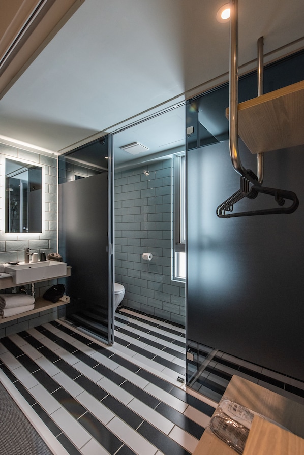 A modern bathroom with a glass shower enclosure, a black and white striped floor, and a wooden vanity with a mirror. - Hotel Ramble (Taichung)