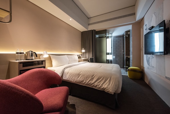 A modern hotel room with a large bed, a desk with a lamp, a TV mounted on the wall, and a shower area visible through a glass door. - Hotel Ramble (Taichung)