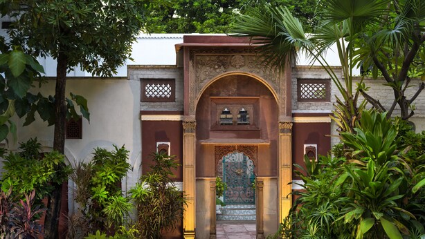 A pathway leading to a traditional building with an ornate entrance, surrounded by lush greenery and a tiled walkway. - Nivah (Moradabad)