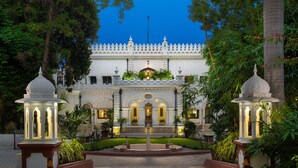 A grand entrance with a symmetrical garden, white ornate architecture, and two illuminated lanterns. - Nivah (Moradabad)