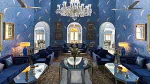 A luxurious room with a blue patterned wallpaper, a chandelier, and blue furniture. - Nivah (Moradabad)