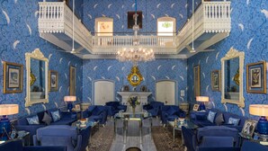 A room with blue patterned wallpaper, a chandelier, and blue upholstered furniture. - Nivah (Moradabad)