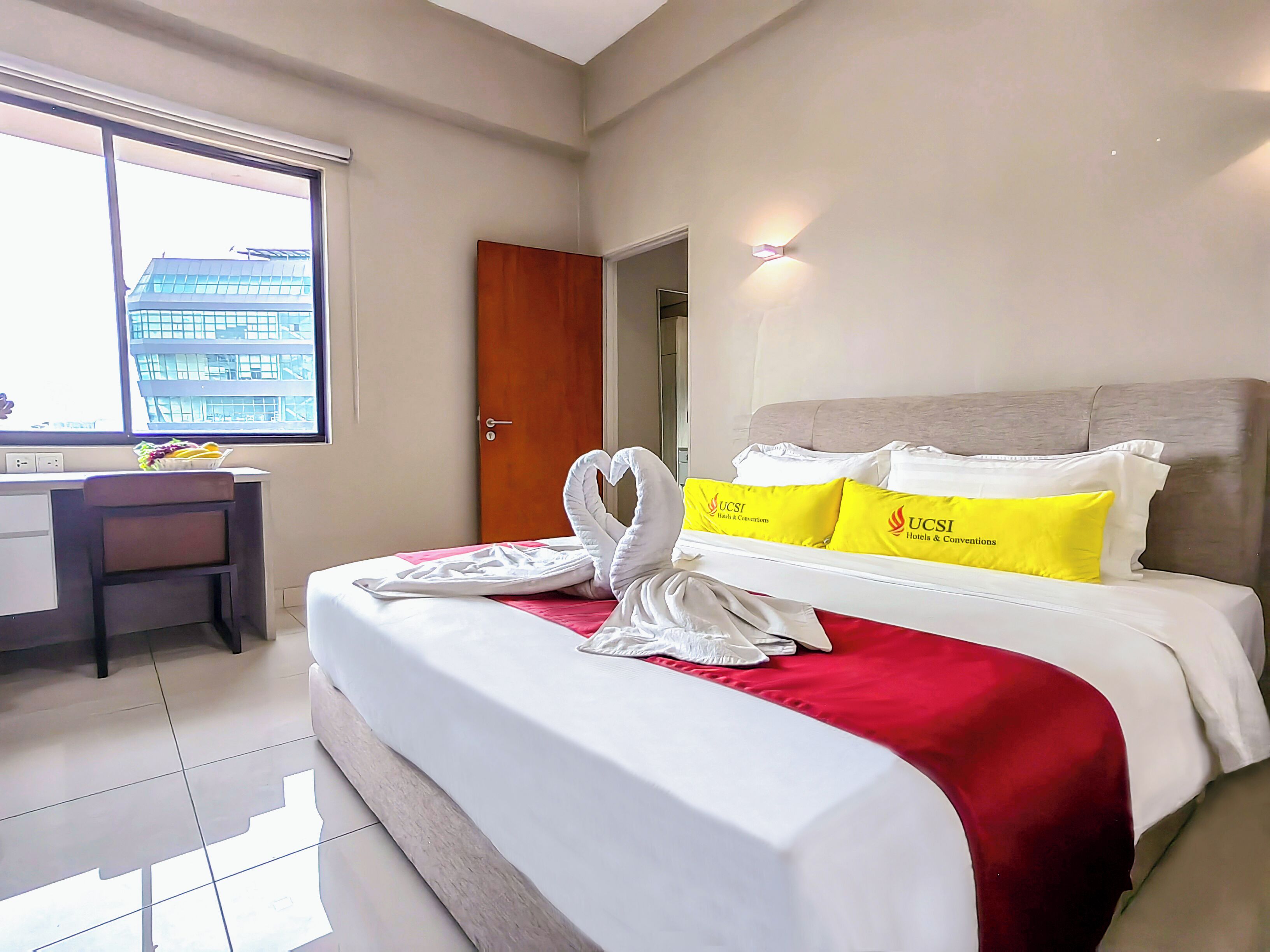 A hotel room with a bed, a desk, and a window with a view of a building.