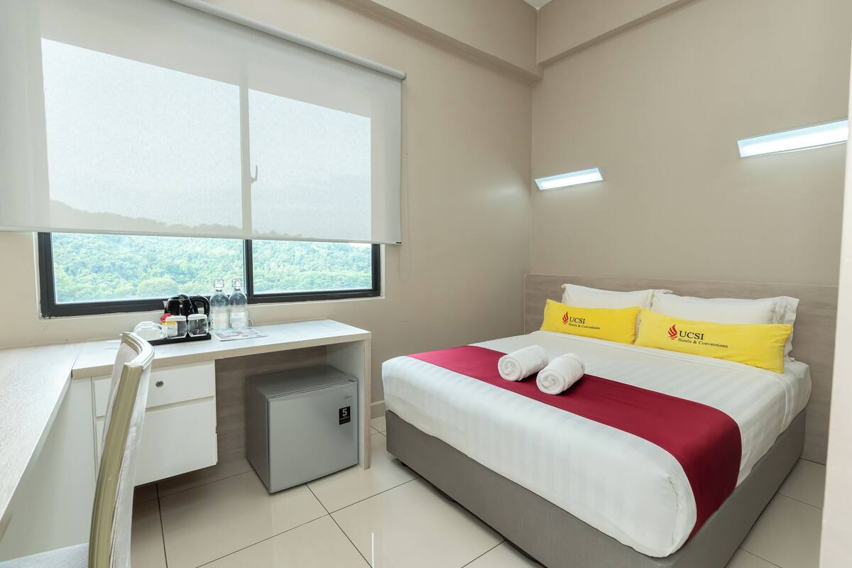 A hotel room with a bed, a desk, and a window.