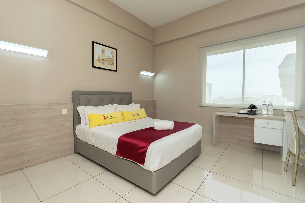 A modern hotel room with a bed, a desk, and a large window.