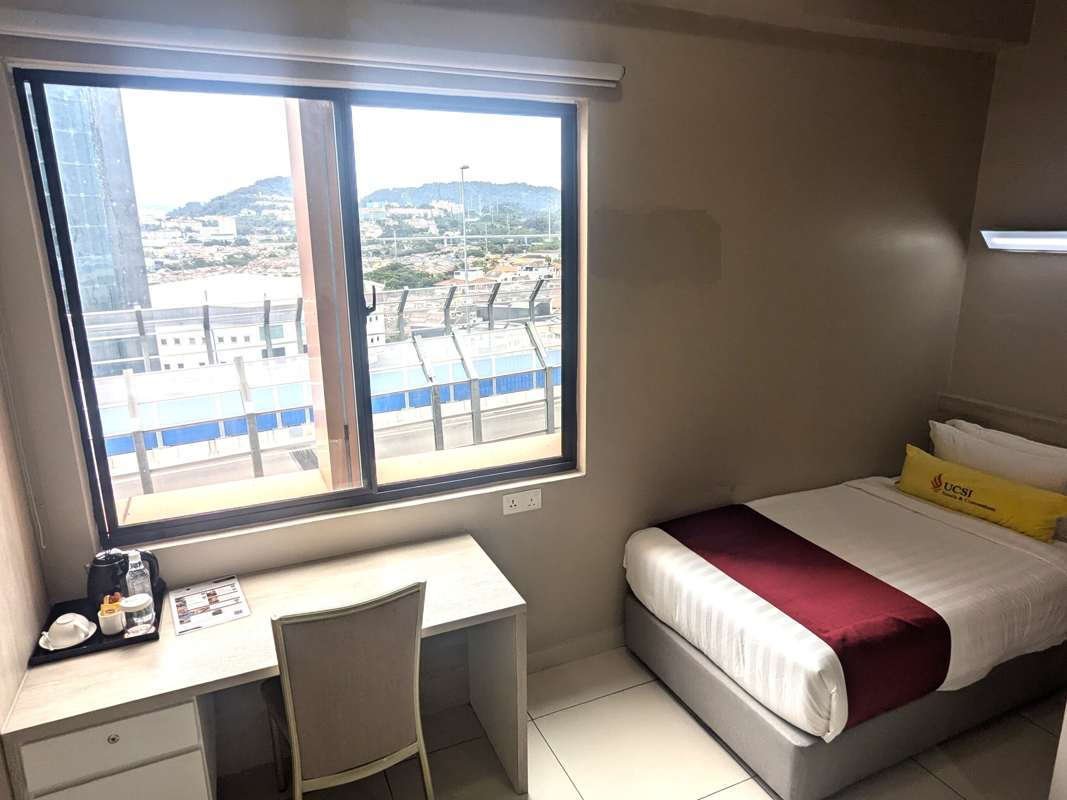 A hotel room with a desk, chair, and a bed with a yellow pillow.