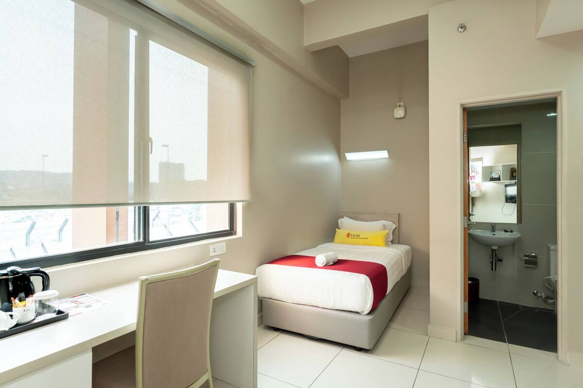 A hotel room with a bed, desk, chair, and a bathroom visible through an open door.