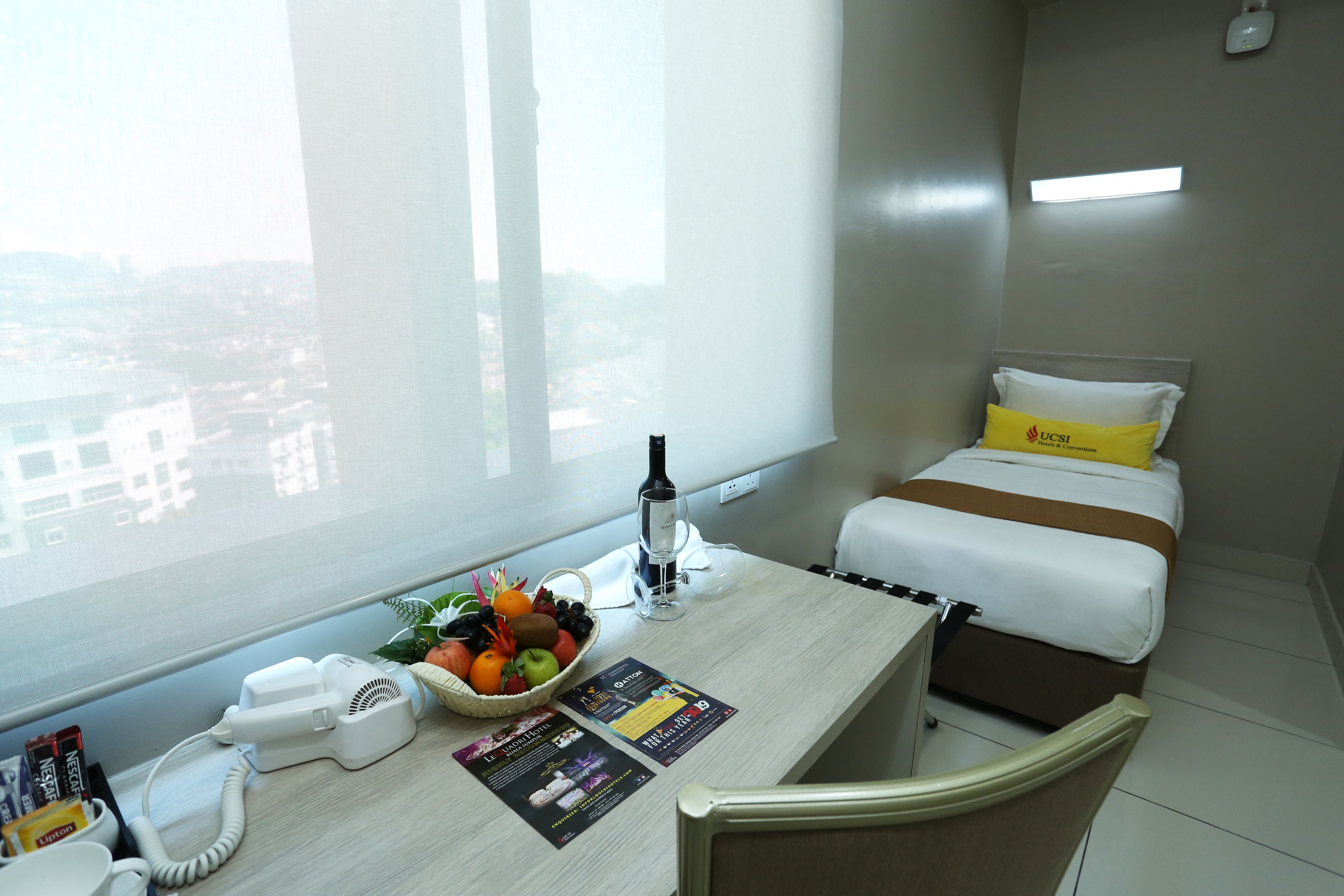 Habitación de hotel con cama, escritorio con teléfono, cesta de fruta y ventana con vista a la ciudad.