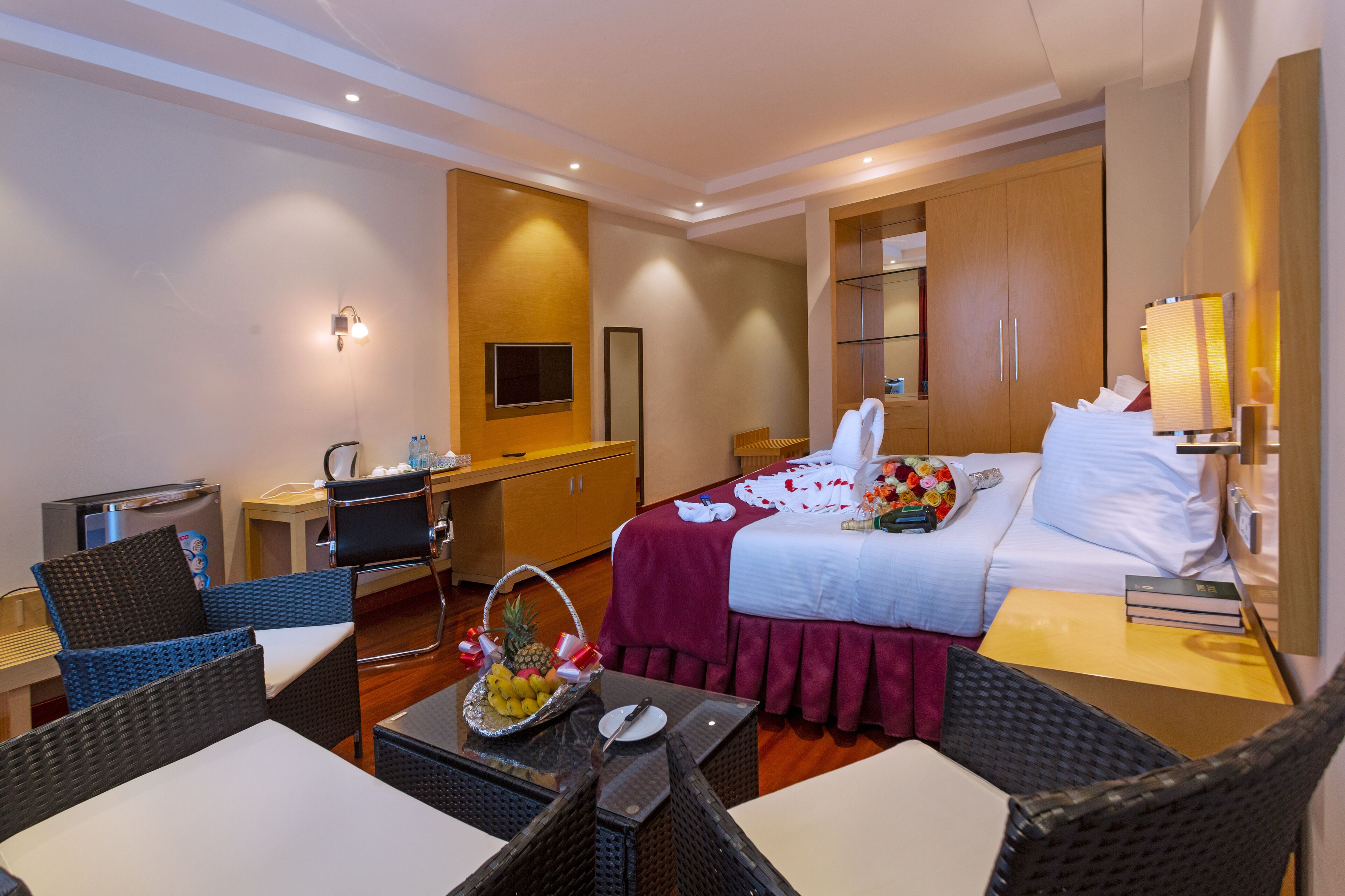 Een hotelkamer met een bed, een bureau, een stoel, een tafel met een fruitmand en een televisie.