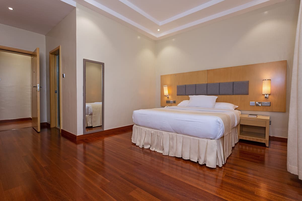 A hotel room with a large bed, wooden headboard, bedside lamps, and a mirror.