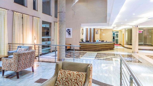 A spacious lobby with a reception desk, seating area, and a large pillar. - Three Steers Hotel (Meru)