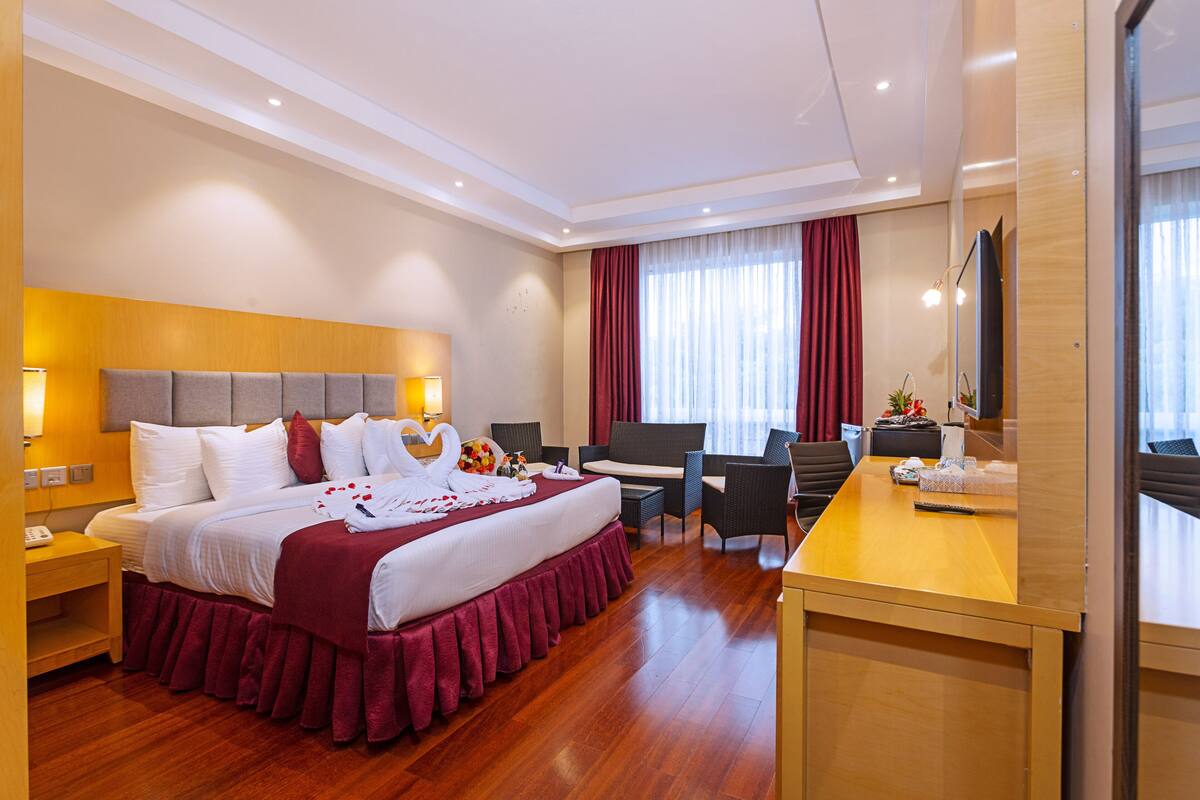 A hotel room with a large bed, a desk, a chair, and a TV.