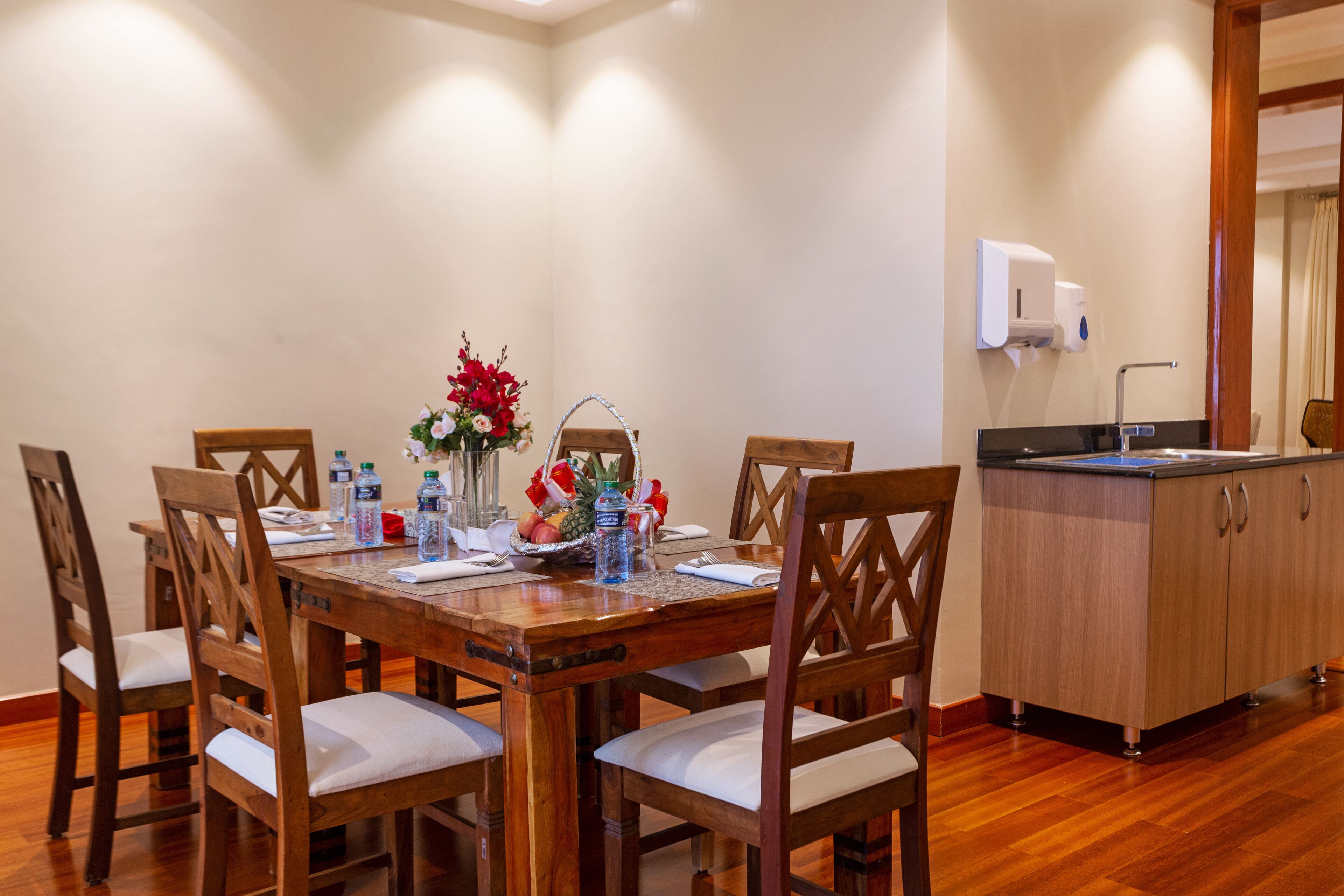 A wooden dining table with six chairs, a vase with flowers, and a fruit basket.