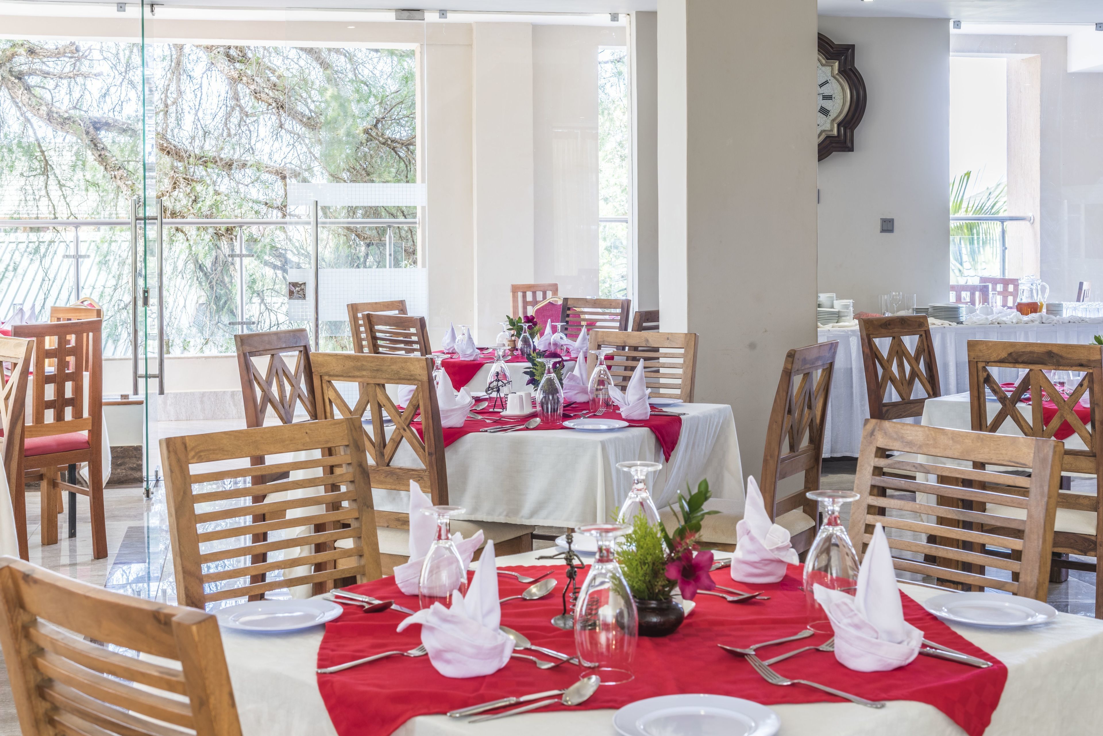 A dining area with tables set for a meal, featuring wooden chairs and a red tablecloth.