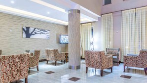 A lobby with patterned chairs, a large pillar, a flat-screen TV, and a tree painting on the wall. - Three Steers Hotel (Meru)