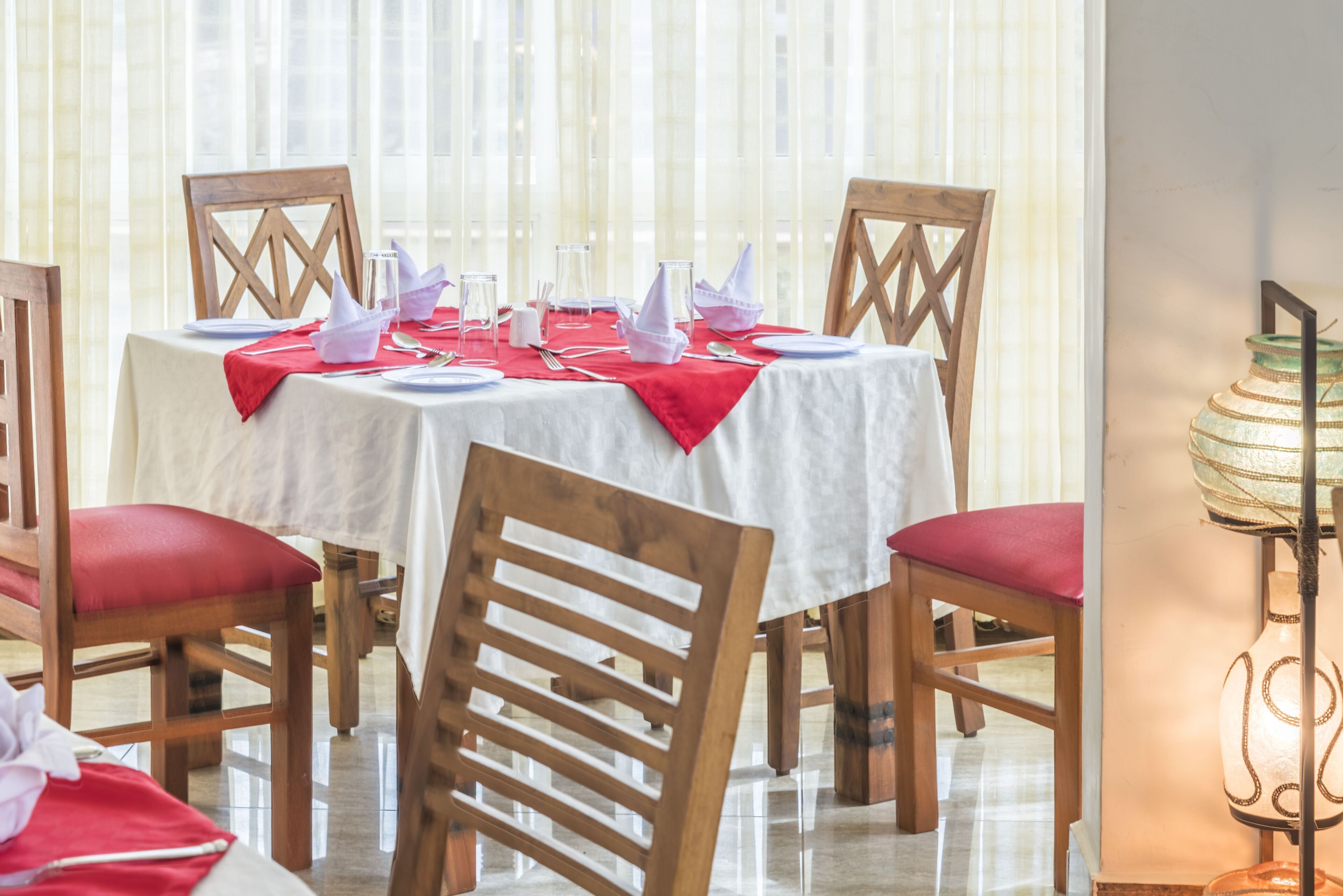 A dining area with a round table set for four, surrounded by wooden chairs with red cushions.