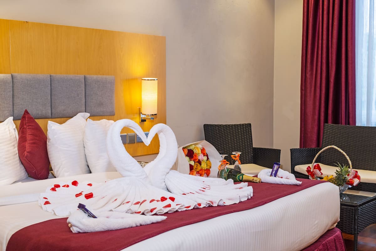 A hotel room with a bed, a nightstand, a lamp, a window with curtains, and a wall with a wooden panel.