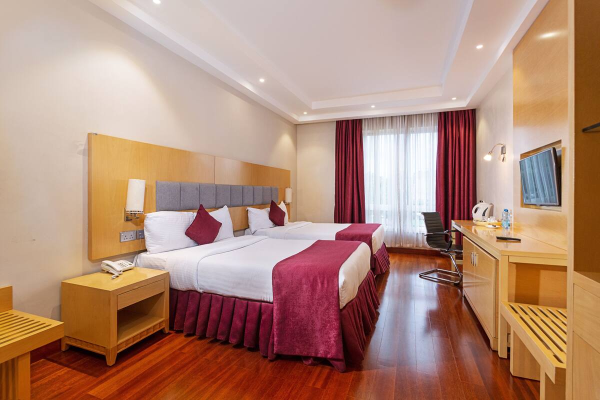 A hotel room with two beds, a desk, a chair, a phone, and a TV.