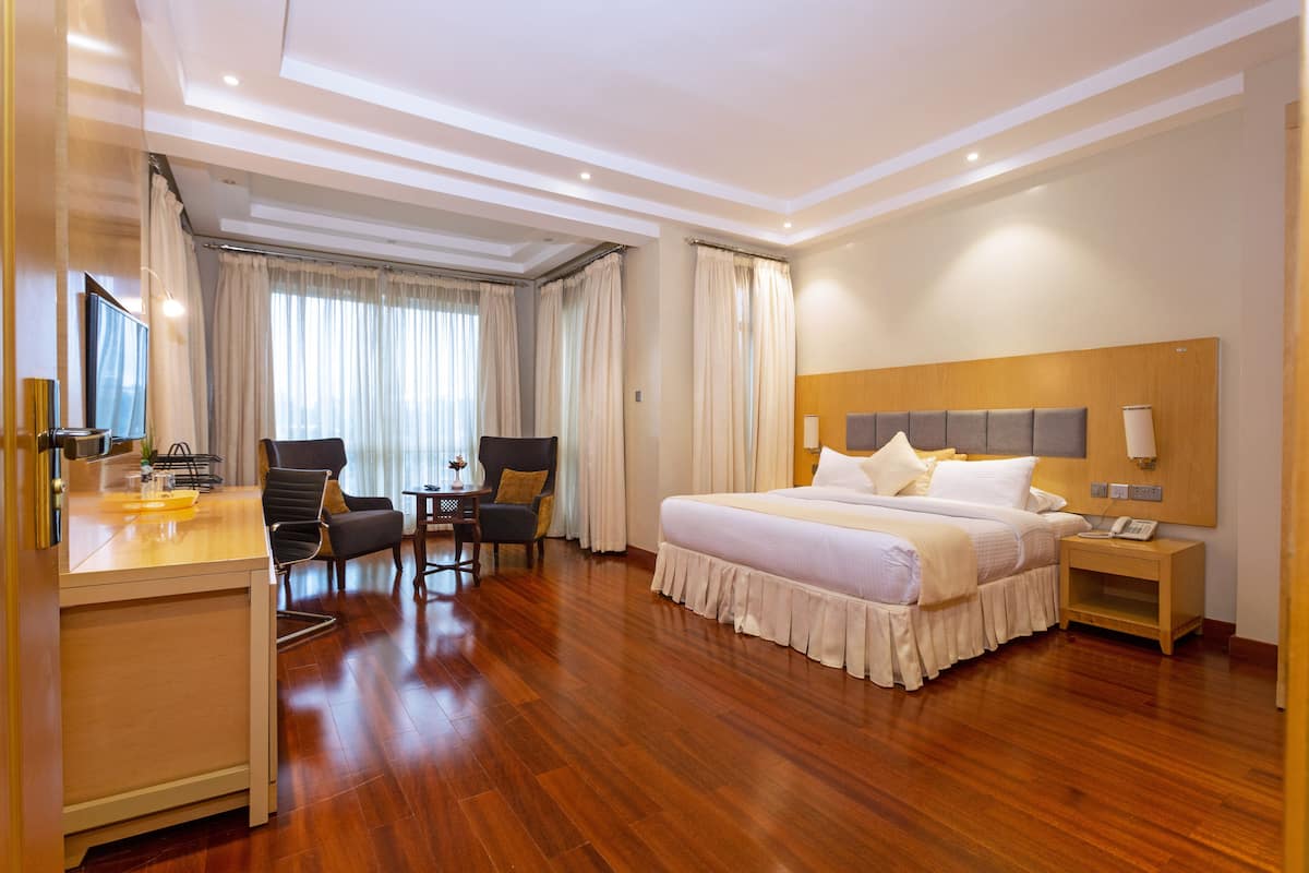 A hotel room with a large bed, a desk with a chair, a small table, and a TV.