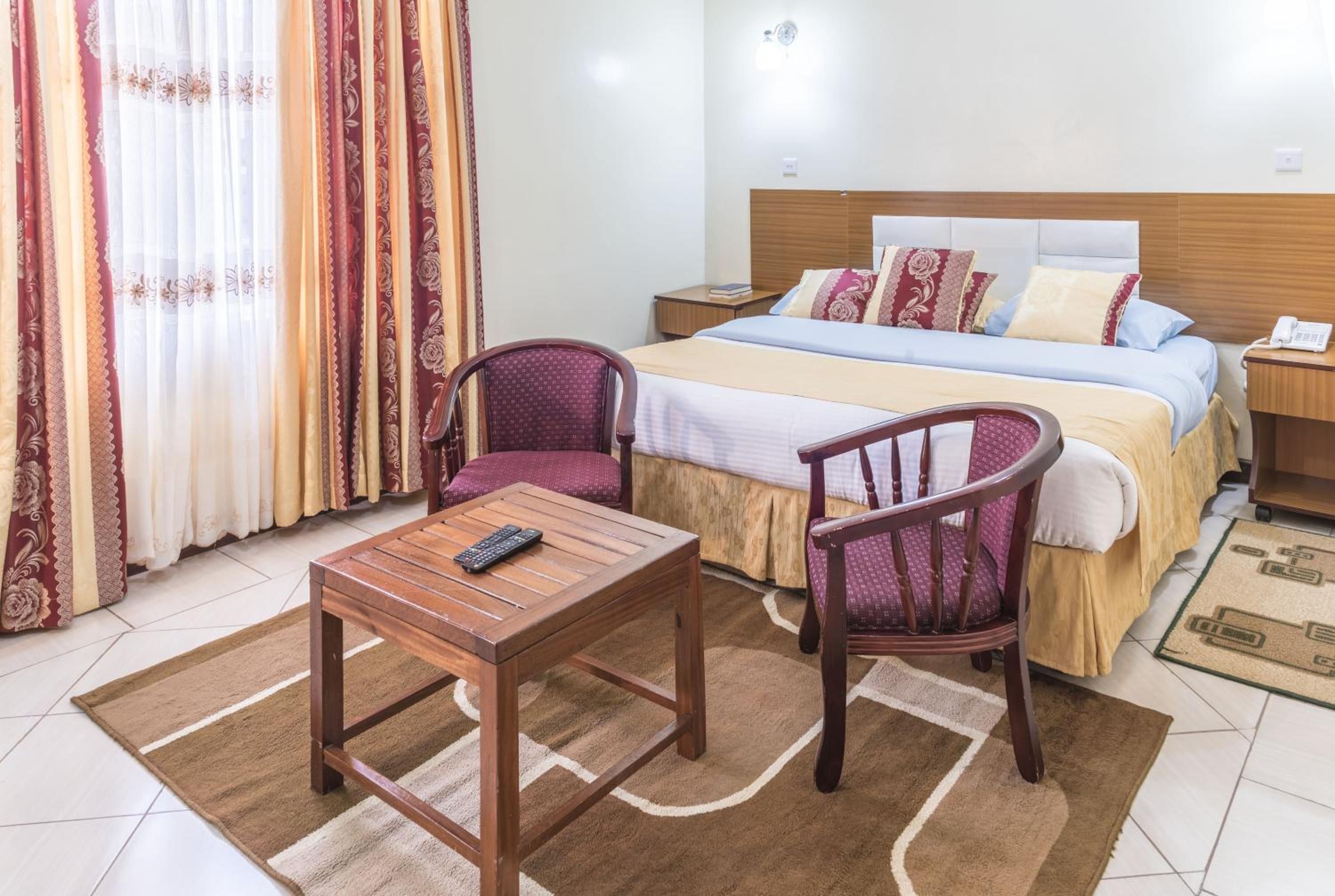 Une chambre d’hôtel avec un lit, deux chaises, une table de chevet et une petite table de nuit, ainsi qu’une télécommande posée sur la table.