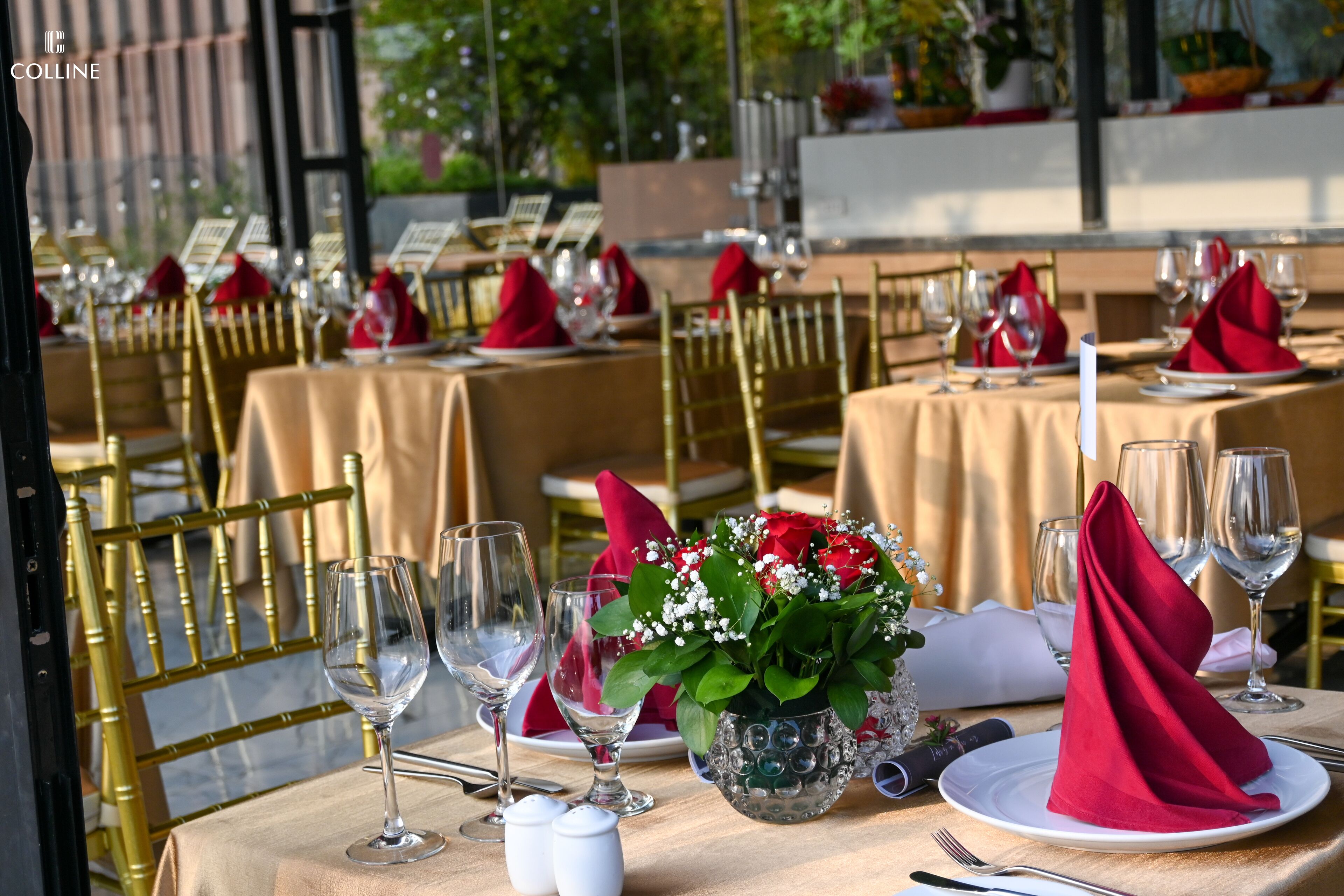 A restaurant setting with tables set for dining, featuring gold chairs, white plates, and red napkins.