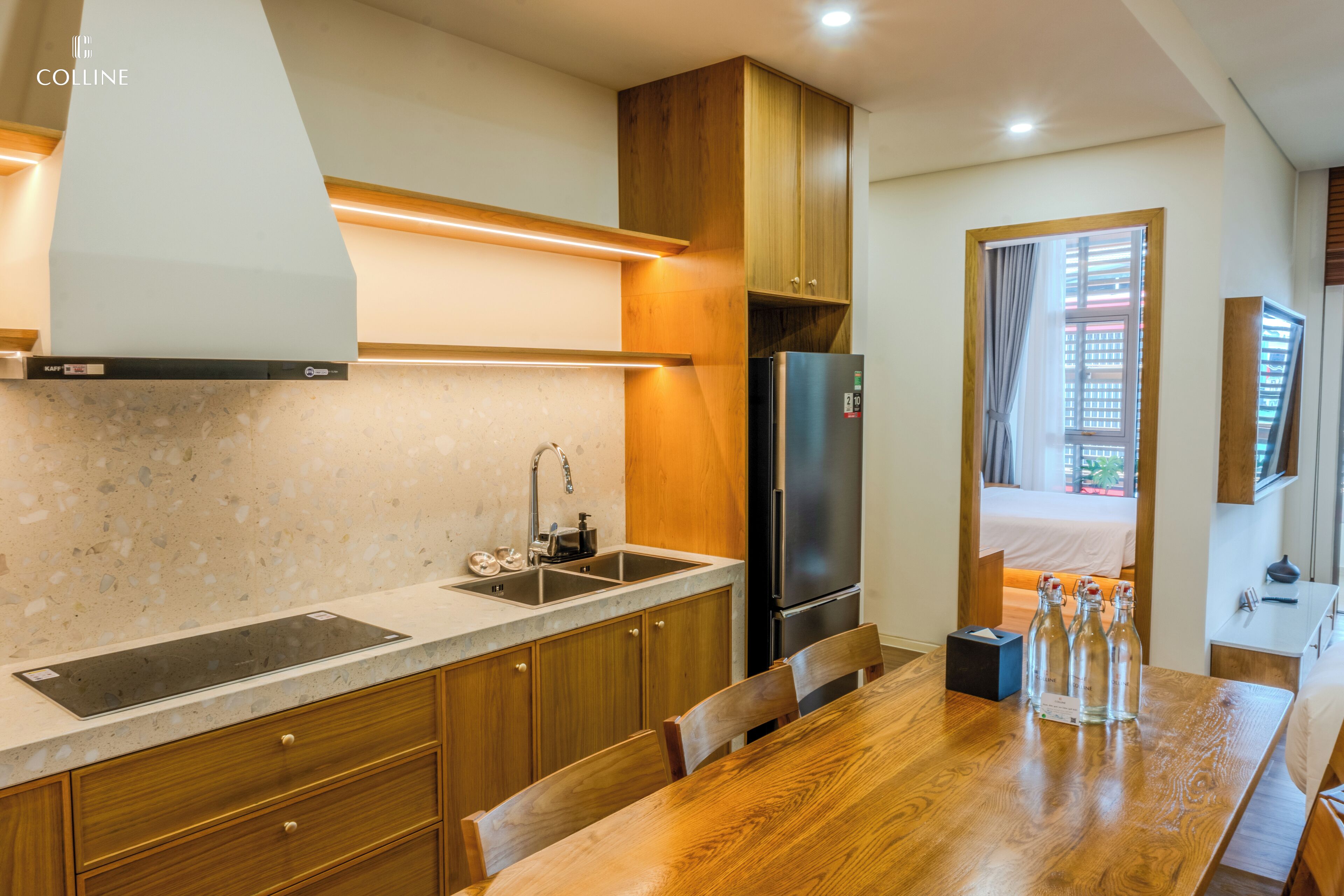 A compact kitchen with a built-in stove, sink, and refrigerator. There is a dining table with chairs and a small window with curtains.