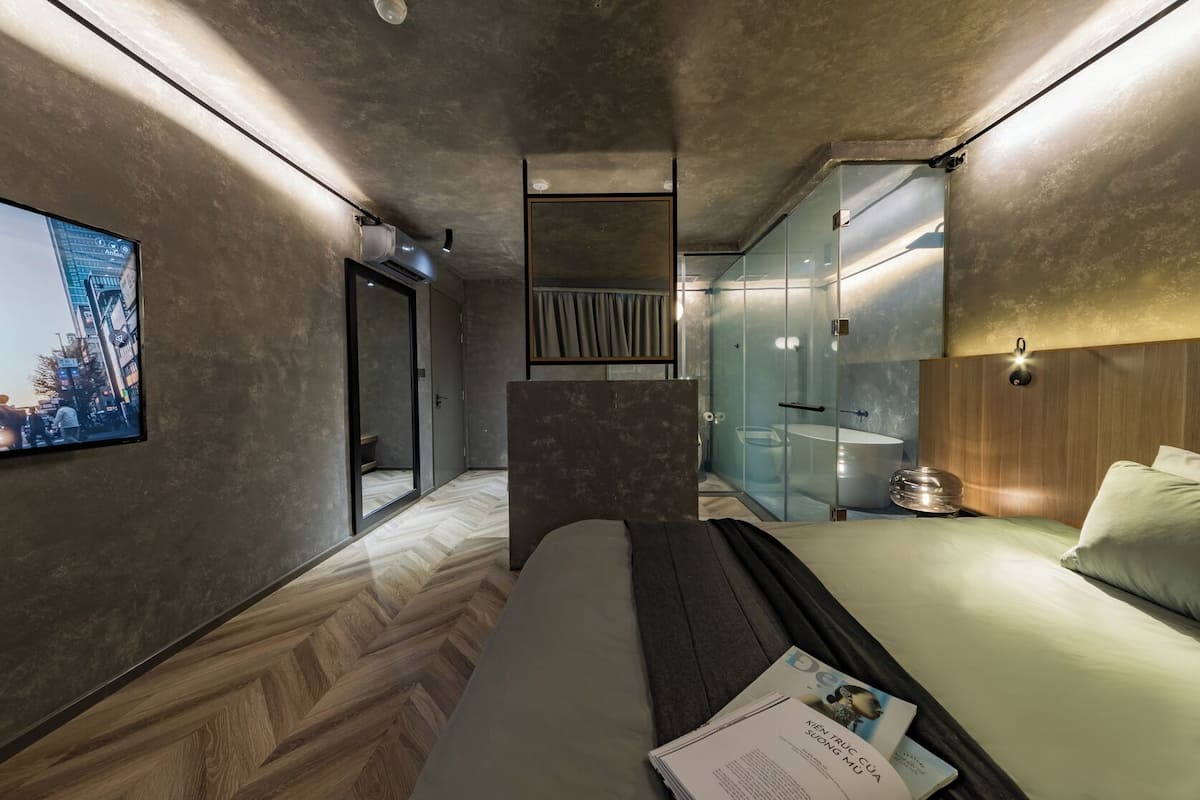 A modern hotel room with a bed, a desk, a glass-enclosed shower, and a cityscape view on the wall.