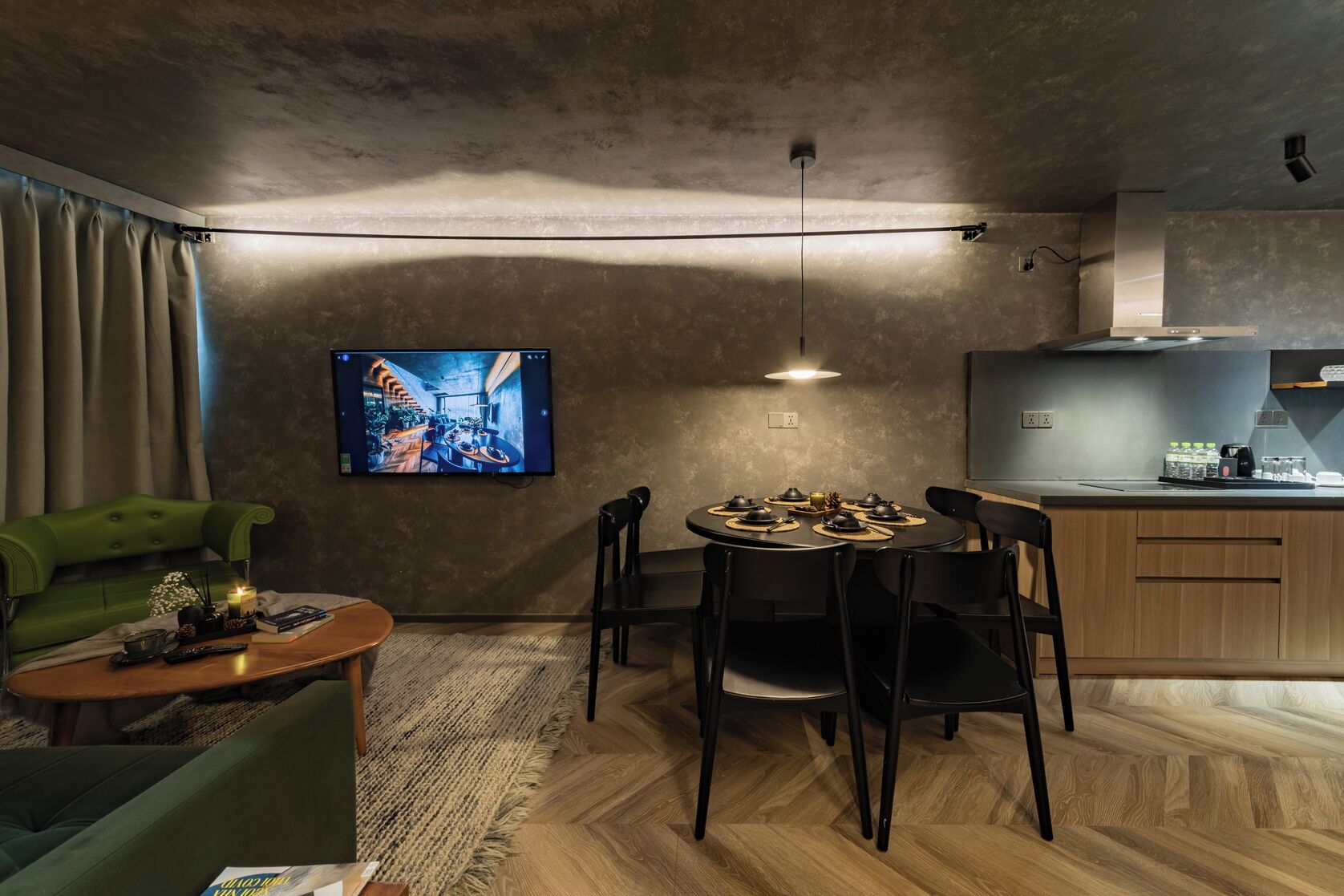 Un salon moderne comprenant un coin repas, un canapé vert, une table basse et un téléviseur fixé au mur.