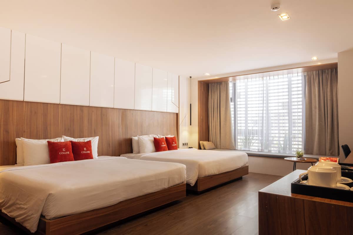 A hotel room with two beds, wooden headboard, large window with curtains, and a small table with a plant.