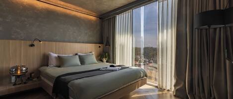 Un dormitorio moderno con una cama grande, una mesita de noche, una lámpara y vistas de la ciudad a través de amplios ventanales.