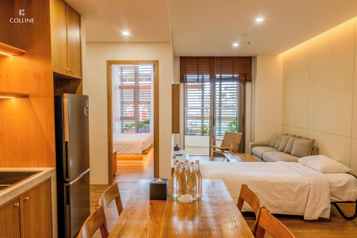 A compact hotel room with a kitchenette, a bed, a seating area, and a view of the outdoors.