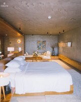 Une chambre à coucher moderne avec un grand lit, un banc en bois, une petite table et un tableau au mur.