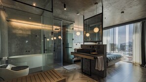 A modern bedroom with a large window, a bedside table, a bed, and a bathroom with a glass shower enclosure. - Colline Dalat (Xuan Huong - Da Lat)