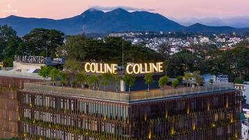 Un edificio con letrero 'Colline', rodeado de árboles y un paisaje montañoso.