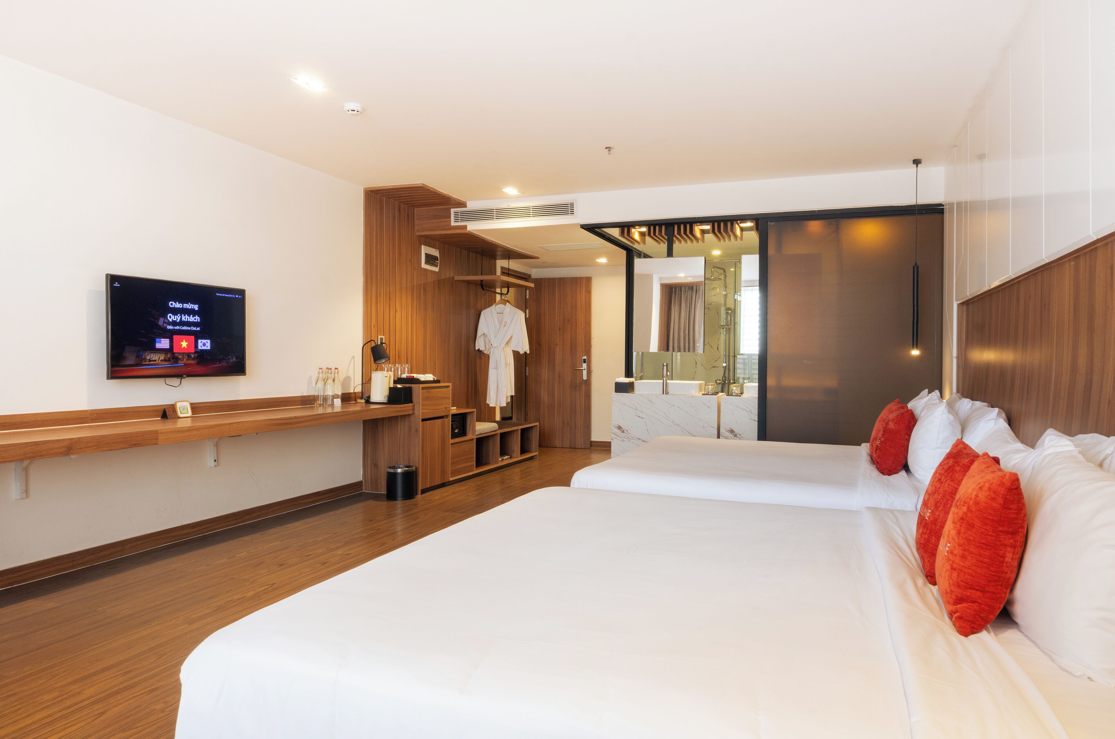 A modern hotel room with a large bed, a TV, a wooden wardrobe, and a bathroom with a glass shower.