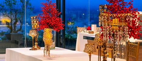 A table with ornate golden vases and candle holders, set against a backdrop of a window with a view of trees and a building.