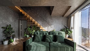 A modern living room with a green sofa, wooden flooring, and a staircase with illuminated steps. - Colline Dalat (Xuan Huong - Da Lat)