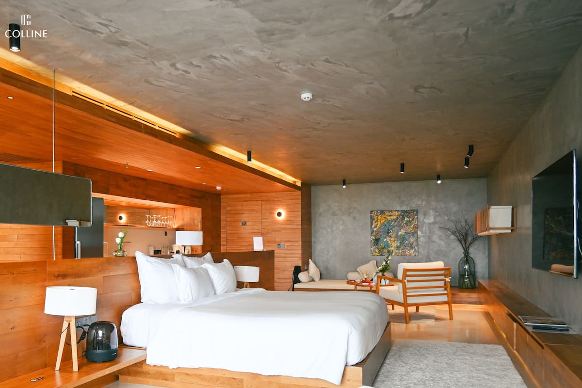 A modern hotel room with a large bed, wooden accents, a flat-screen TV, and a dining area.