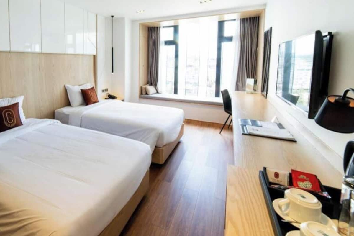 A hotel room with two beds, a desk, a chair, a TV, and a window with a view.
