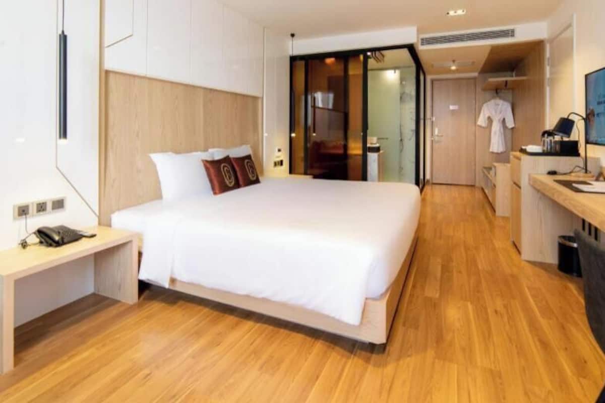 A hotel room with a large bed, a desk, a chair, a TV, and a sliding door leading to a bathroom.