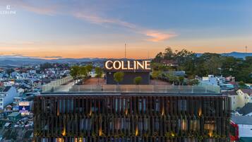 A hotel with a prominent 'Colline' sign, modern architecture, and a view of the surrounding cityscape.