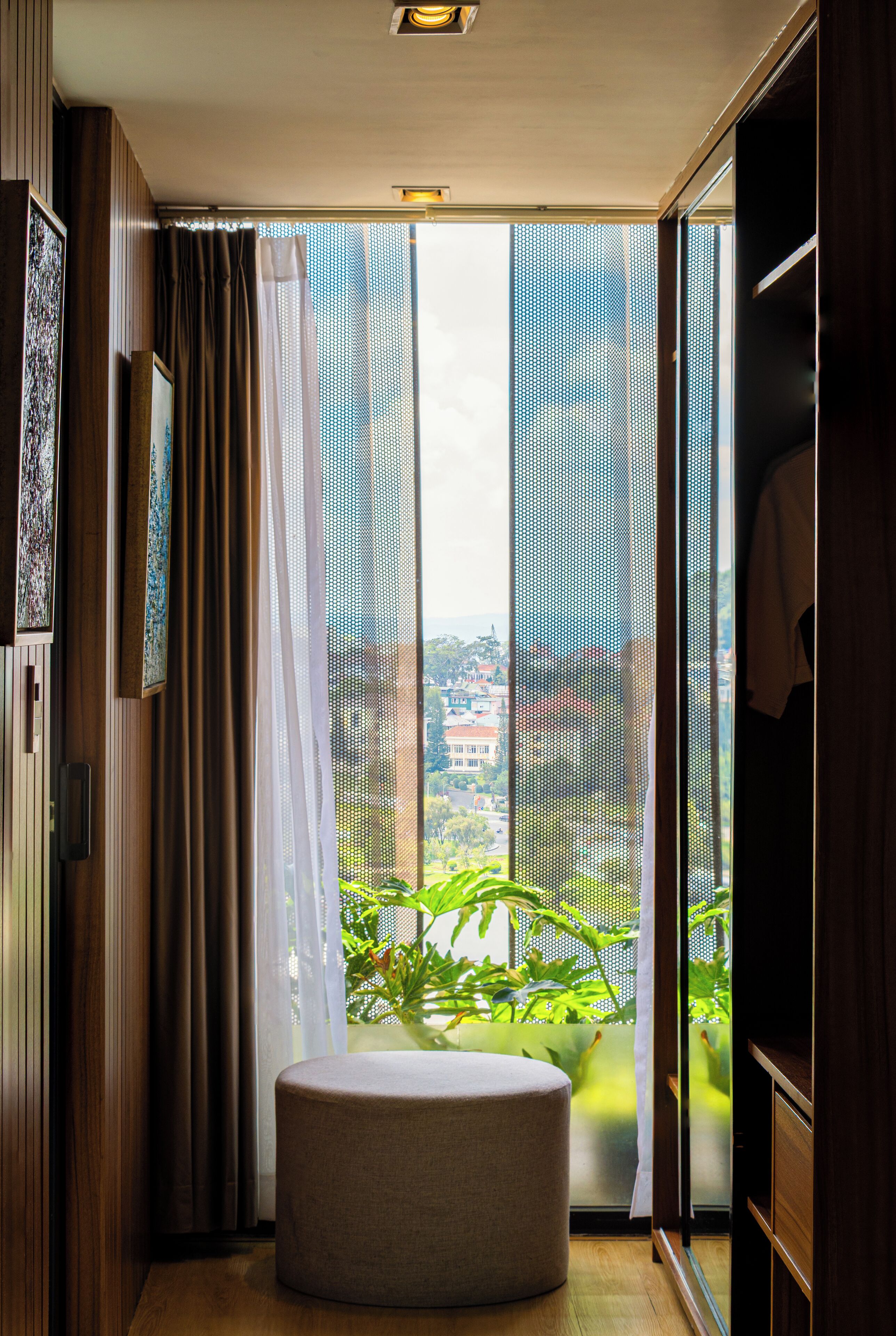 Una habitación moderna con un amplio ventanal corredero que da a un balcón con vistas a un paisaje urbano.