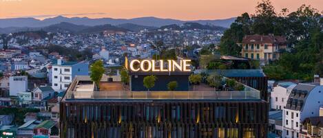 Un hôtel reconnaissable à son grand panneau « Colline », situé au cœur d’une ville et entouré d’un paysage urbain avec des montagnes en arrière-plan.