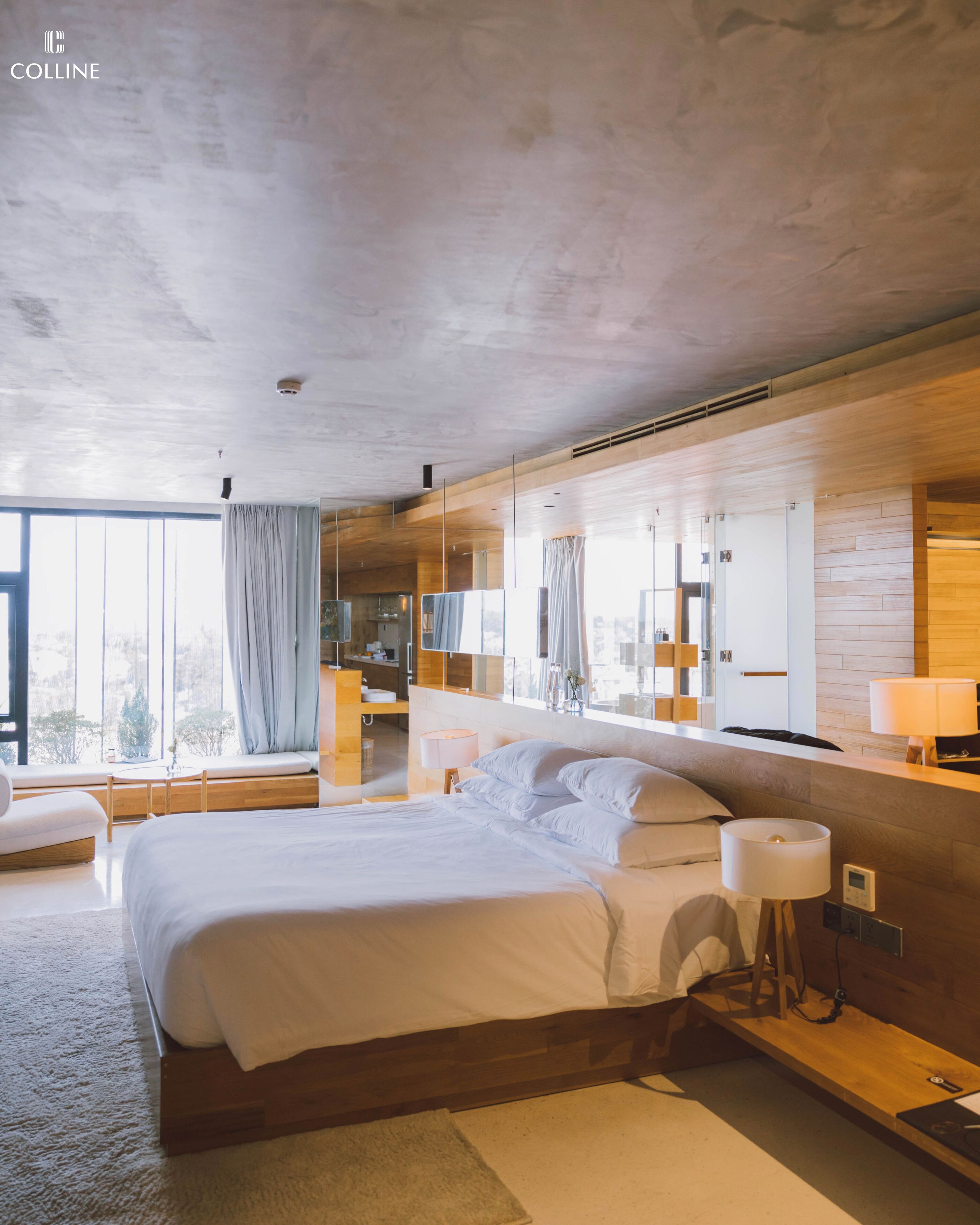 A modern hotel room with a large bed, a sitting area with a view, and a bathroom with a mirror and sink.