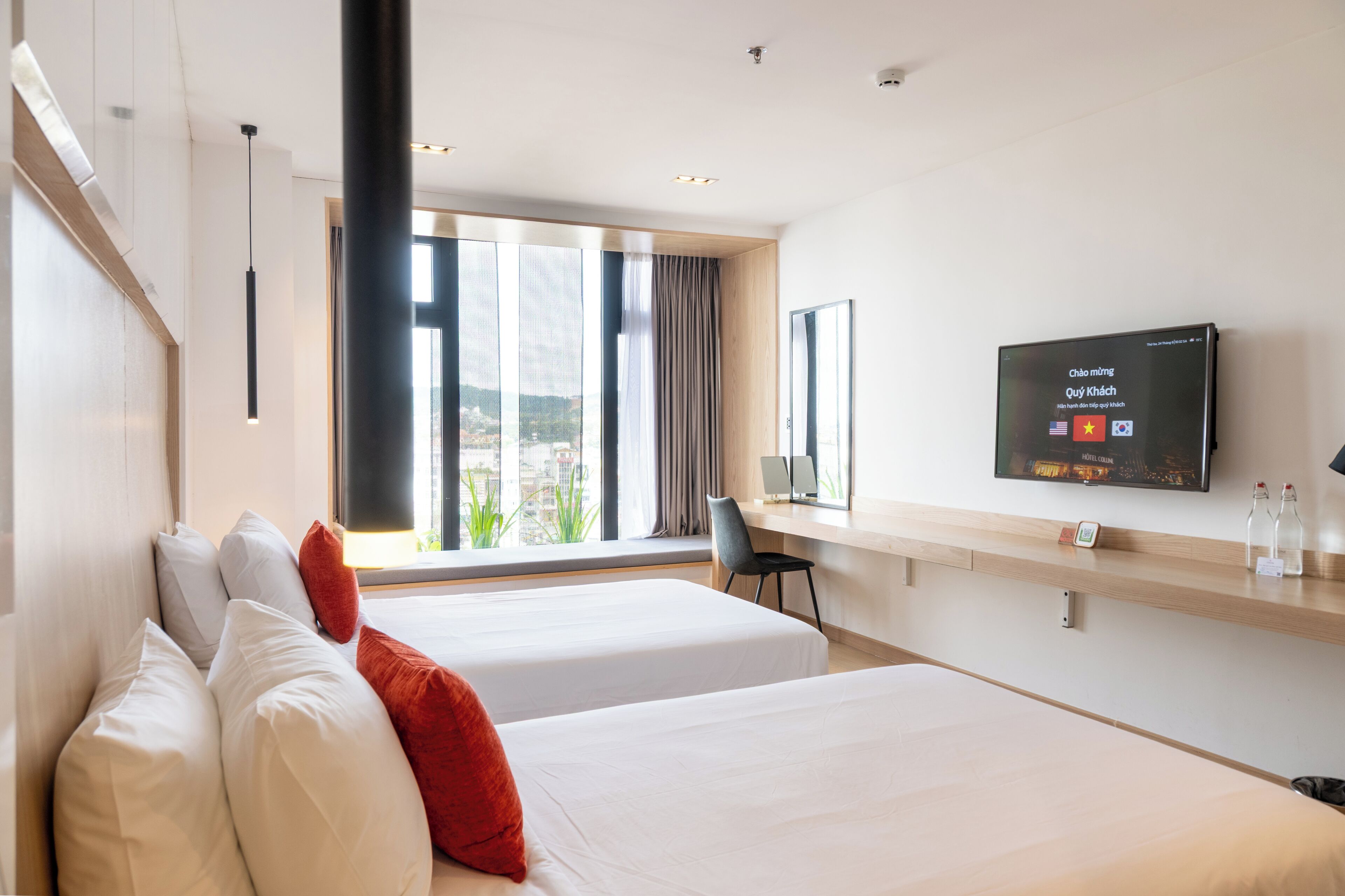 A hotel room with two beds, a desk, a TV, and a large window with curtains.
